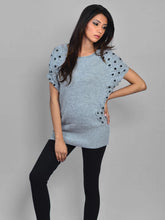 Woman wearing a light blue sweater with black patterns and black leggings on a gray background