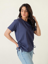 Model wearing Coastline’s Arle Drawstring Side Top in Violet Blue in a standing angled pose, showing the relaxed fit and side drawstring detail.