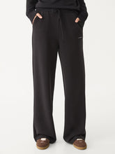 Front view of the Avy black wide-leg trousers showing the relaxed silhouette, with both hands in the pockets.