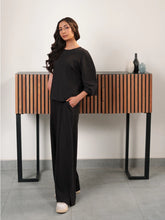 Model wearing The Blair Smoky Black double-knit co-ord set with a relaxed top and wide-leg trousers, with one hand in a pocket.