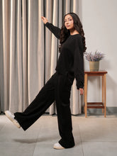 Model wearing the Brooklyn black summer co-ord set with a boxy long-sleeve top and wide-leg trousers, with one leg raised.