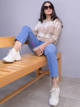 Model seated on a wooden bench wearing the Cathy oversized tie-dye sweatshirt in Almond, blue jeans and white sneakers.