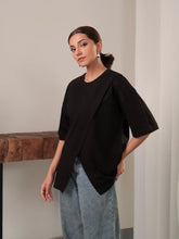 Model wearing Coastline's Cleo Top in Black, showing its oversized boxy fit, short sleeves and split hem, styled with blue wide-leg jeans.