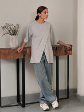 Model wearing Coastline's Cleo Top in Heather Grey with blue wide-leg jeans, showing its oversized boxy fit and split hem.