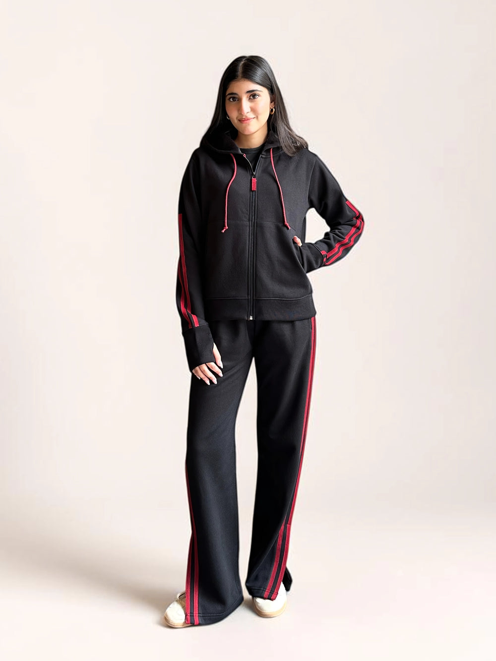 Model wearing Coastline’s black hoodie matching set with red sleeve stripes, red drawstrings and wide-leg trousers with matching side stripes.