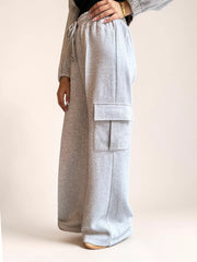Side view of Coastline’s heather gray wide-leg cargo trousers, showing the flap thigh pocket and fleece fabric draping over cream shoes.
