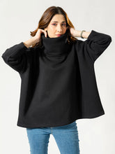 Model wearing the Elkin black high-neck sweatshirt, holding its oversized folded collar with both hands to show the loose, boxy fit.