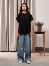 Front view of Coastline's Elle Top in Black, showing its relaxed oversized fit and drop shoulders, styled with light blue wide-leg jeans.