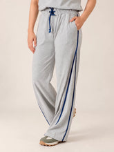 Angled view of the Ellioti Heather Grey flared trousers showing blue contrast piping, a matching drawstring and one hand in a pocket.