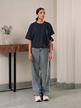 Model wearing Coastline's Jules Top in Oxford Blue, showing its loose silhouette, short sleeves and styling with wide-leg jeans.