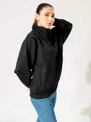 Model wearing the Kai oversized black sweatshirt in a three-quarter pose with one arm raised behind her head.