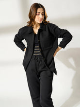 Model wearing the Maru black oversized shacket open over a black top and trousers, with both hands at her waist.