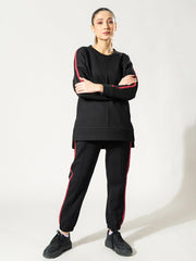 Model wearing the Ora black winter athleisure set with arms crossed, showing the loose top and contrasting sleeve and trouser detailing.