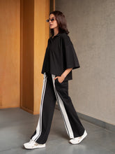 Model walking in the Zane black co-ord set with a loose collared top and wide-leg trousers with contrasting side stripes.