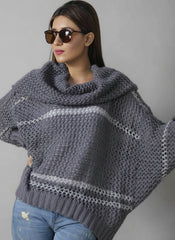 A woman wearing sunglasses and a gray turtleneck chunky sweater with batwing sleeves, standing in front of a newspaper print background.