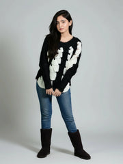 Woman wearing a black sweater with white patterns, blue jeans, and black boots on a gray background