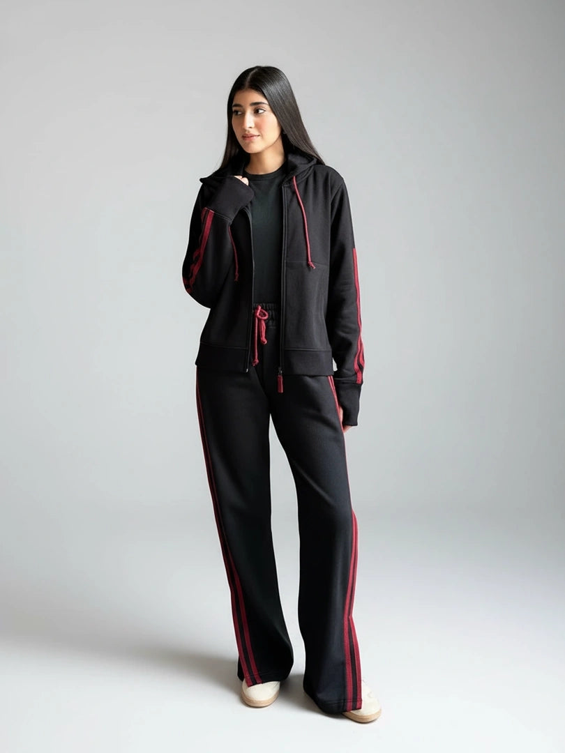 Person wearing a black tracksuit with red accents on a plain background