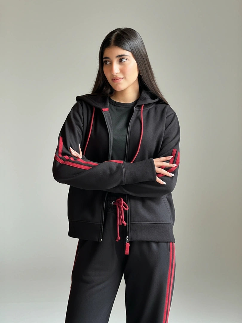 Person wearing a black tracksuit with red accents on a plain background