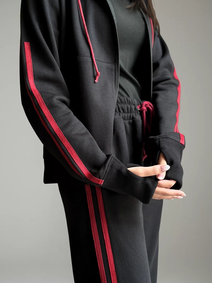 Black tracksuit with red accents worn by a person on a gray background