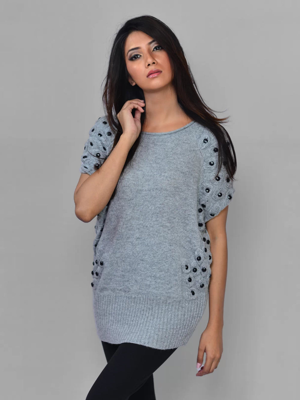 Woman wearing a gray sweater with black embellishments on a gray background