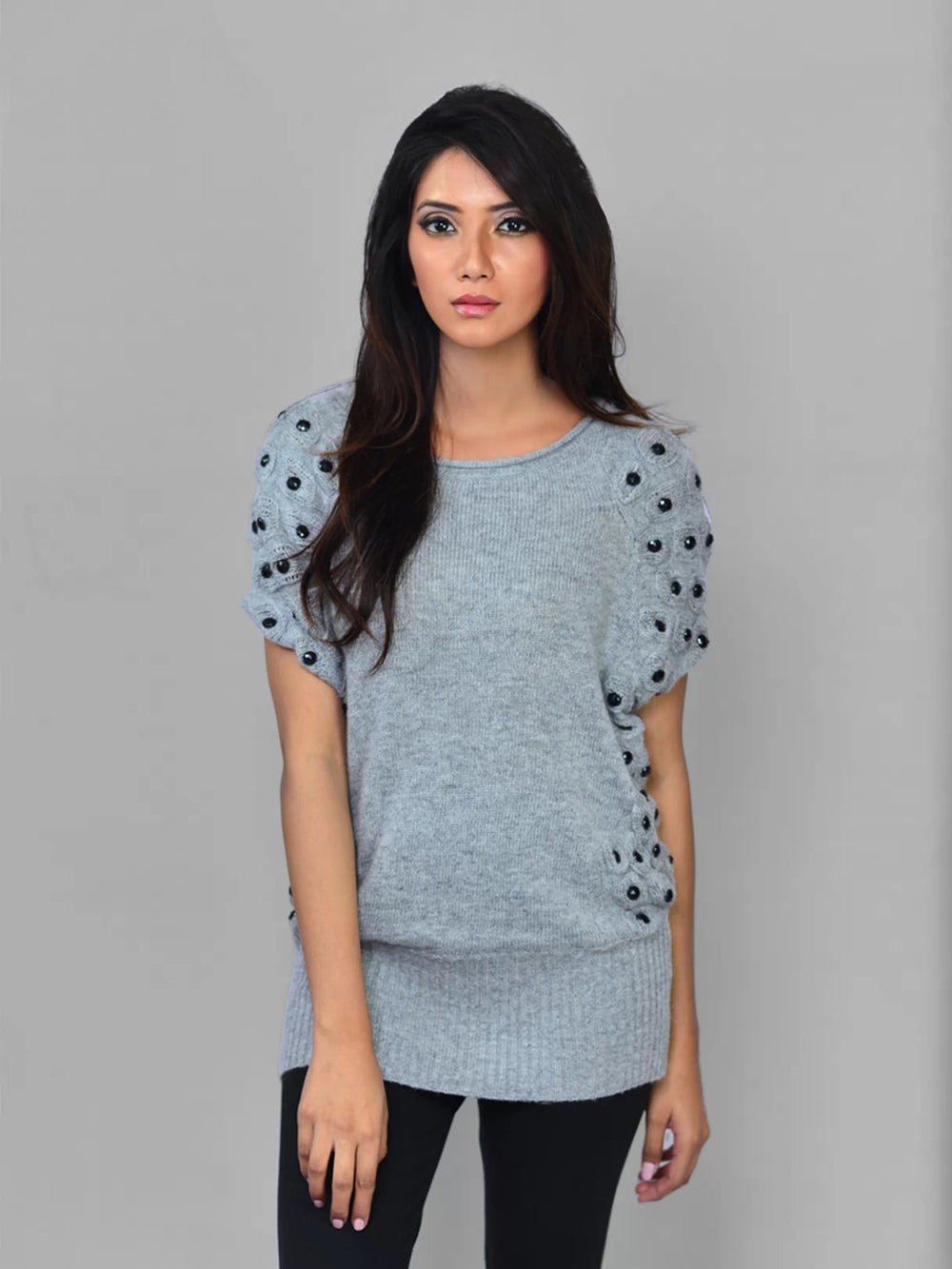 Woman wearing a light blue sweater with black embellishments on a gray background