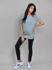 Woman wearing a light blue sweater with black patterns and black leggings on a gray background