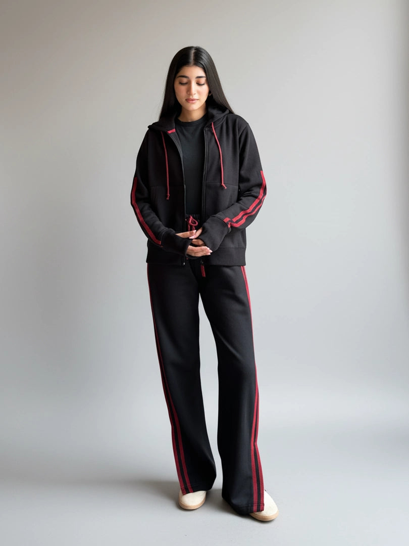 Person wearing a black tracksuit with red accents on a plain background