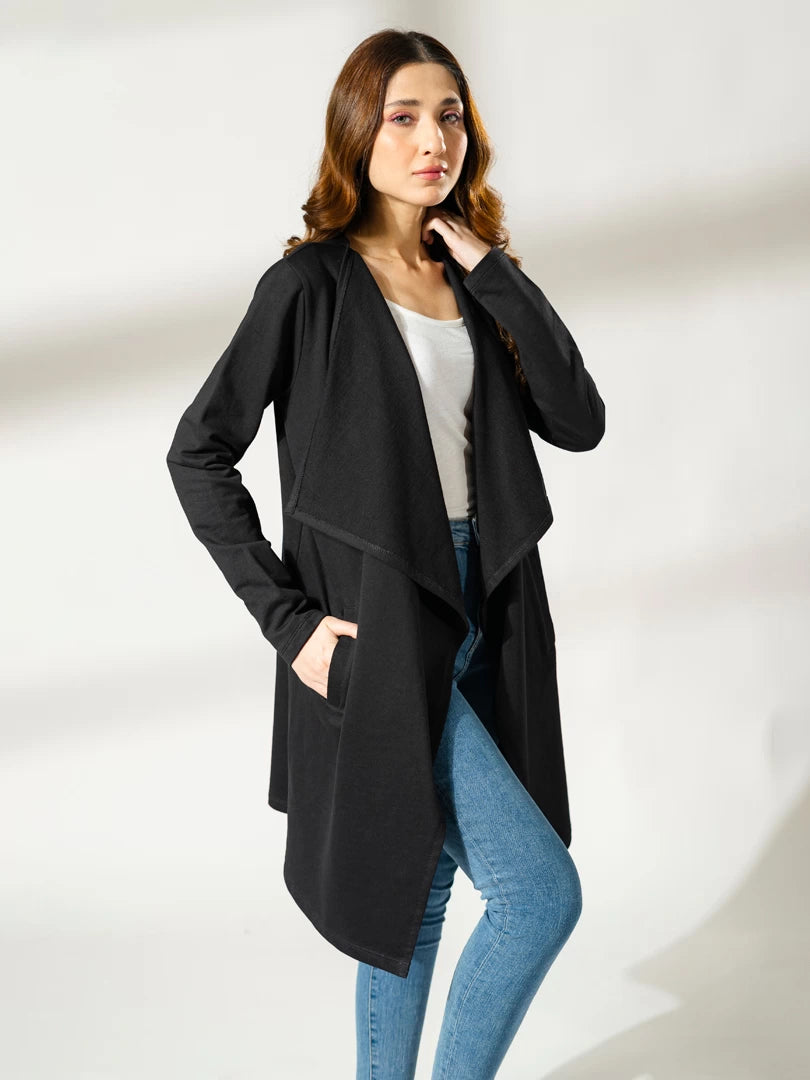Model wearing the Ashley black draped overlayer with one hand at her hip, showing the open front and asymmetric hemline.