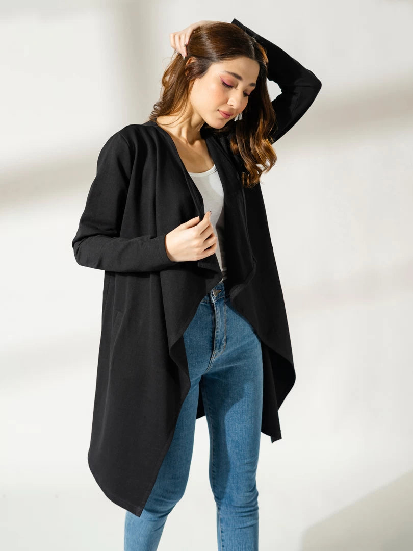 Model wearing the Ashley black long-sleeve overlayer with one hand raised to her hair and the other holding the front edge.