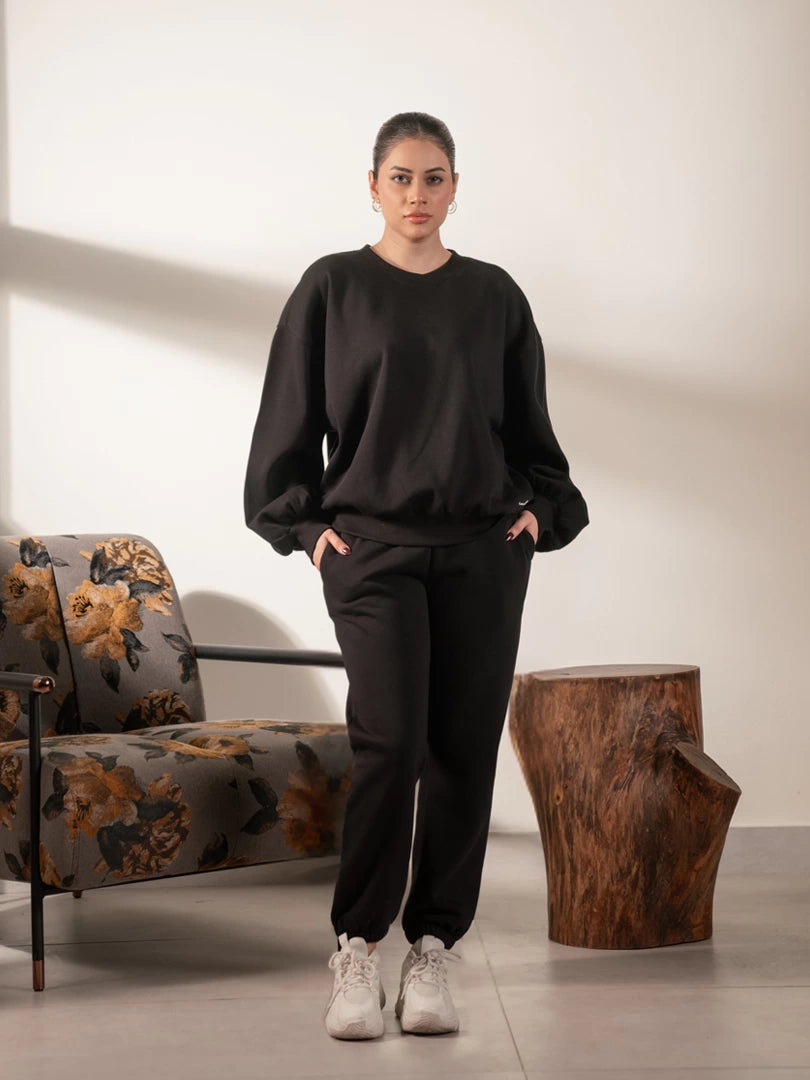 Full-length studio view of the Barlow oversized black sweatshirt with balloon sleeves, styled with black trousers and white sneakers.