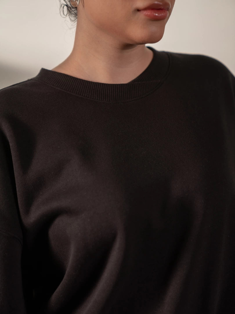 Close-up of the Barlow oversized black sweatshirt showing its distinctive twisted rib crew neckline and smooth fleece fabric.