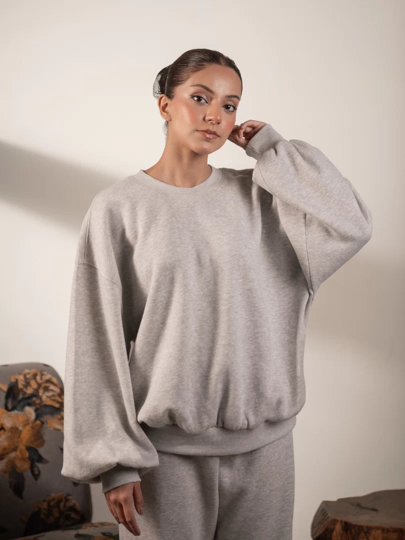 Model wearing the Barlow oversized sweatshirt in Heather Grey, with one hand raised near her face and the balloon sleeves clearly visible.
