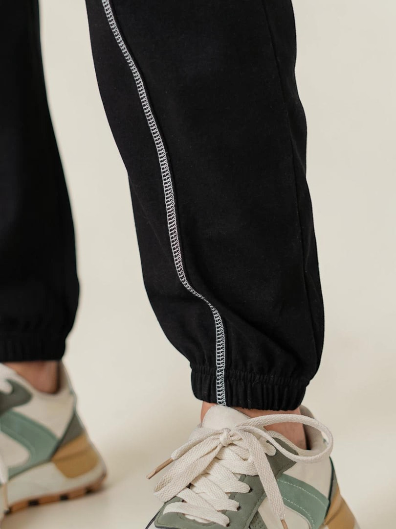 Close-up of the Berlin Black trousers showing the contrast side stitching and elasticated ankle hems.