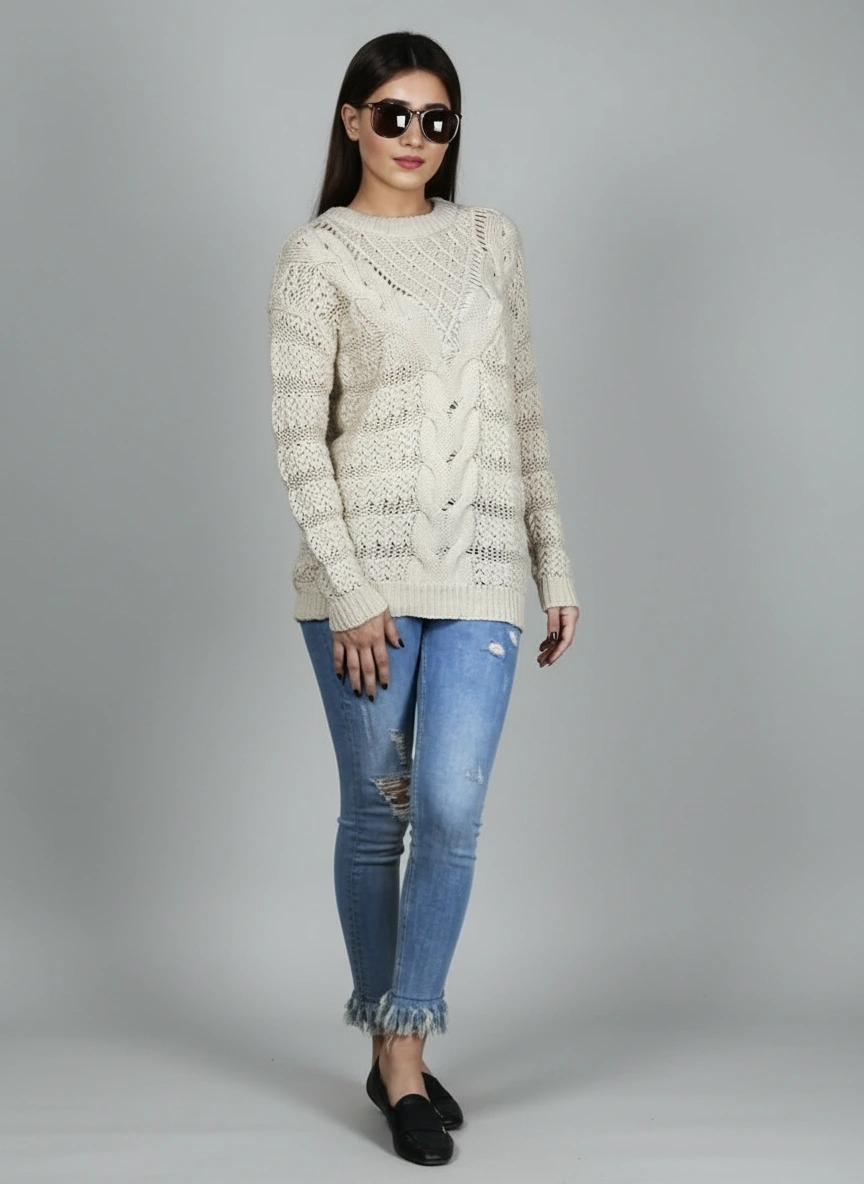 Angled standing view of Coastline's Ivory Cable Knit Sweater with textured cable-knit design, styled with blue jeans.