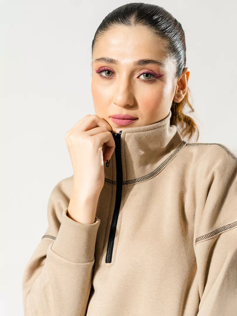 Model wearing the Calca Natural Sand sweatshirt showing the high standing collar and short front zipper