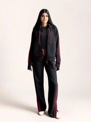 Front view of a model wearing Coastline’s black and red hoodie set, showing the relaxed jacket fit and full-length wide-leg trousers.
