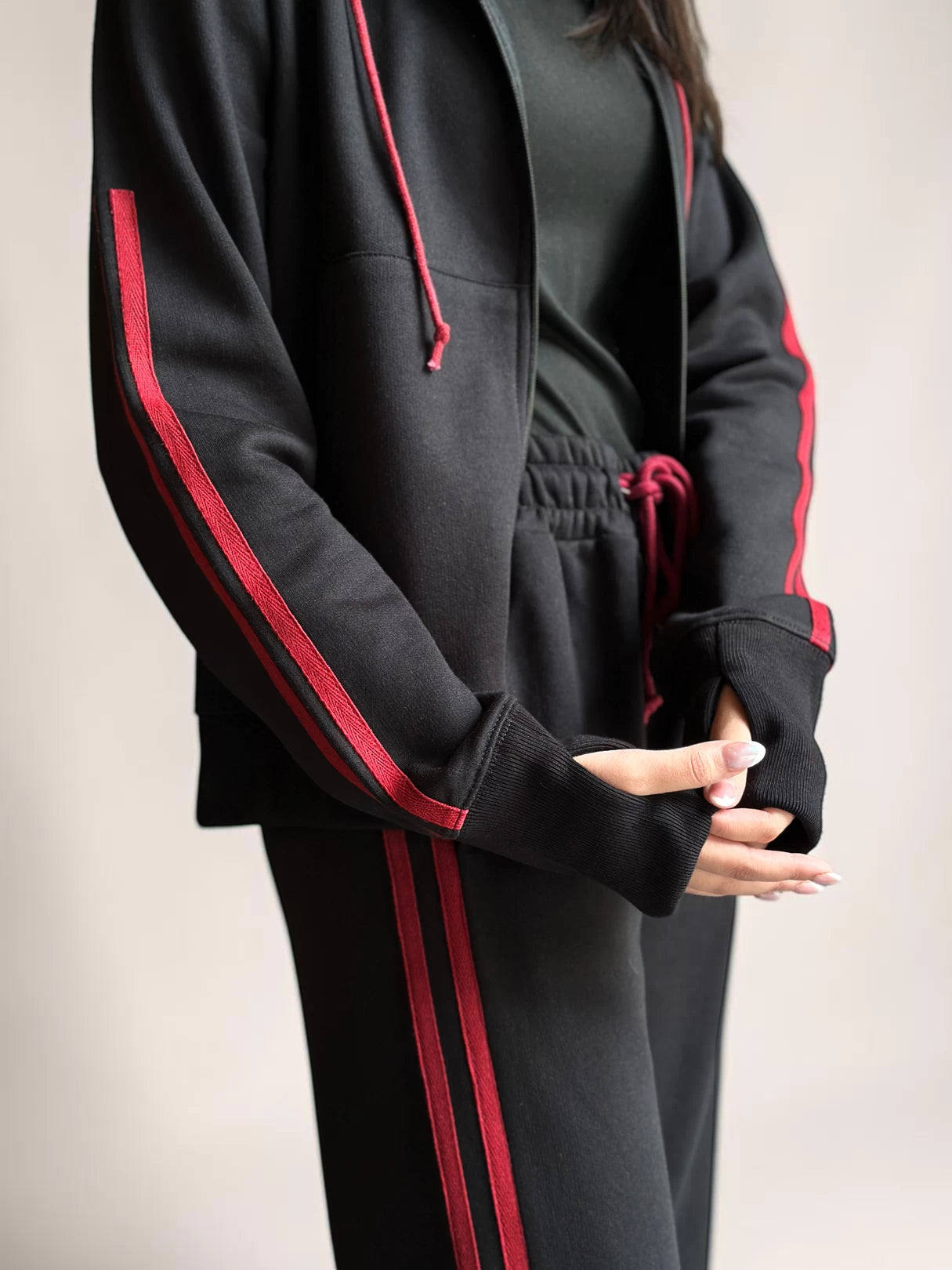 Close-up of Coastline’s black hoodie showing the front zipper, red drawstrings, red sleeve stripes and front pocket detail.