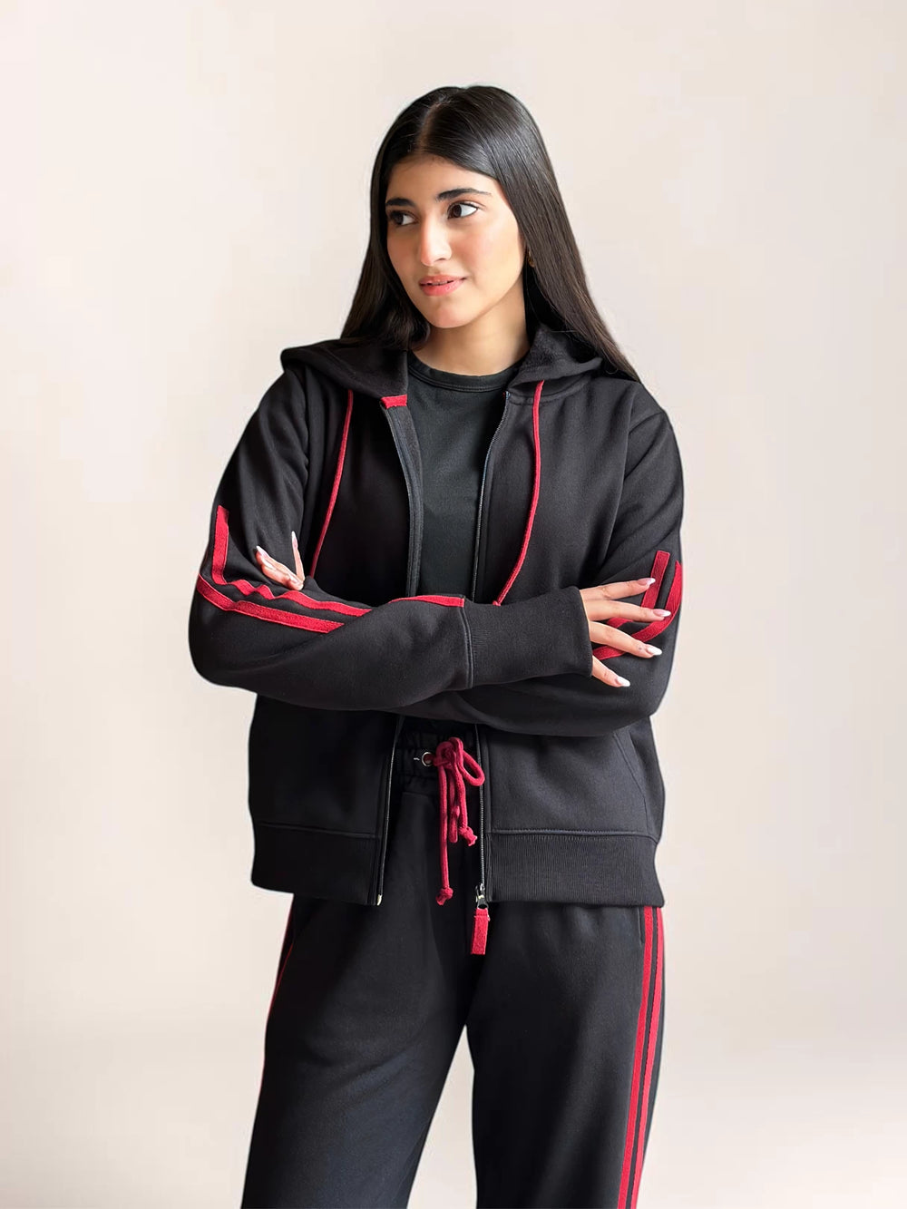 Model wearing Coastline’s black zip-front hoodie with her arms crossed, showing the red sleeve stripes, hood and drawstrings.