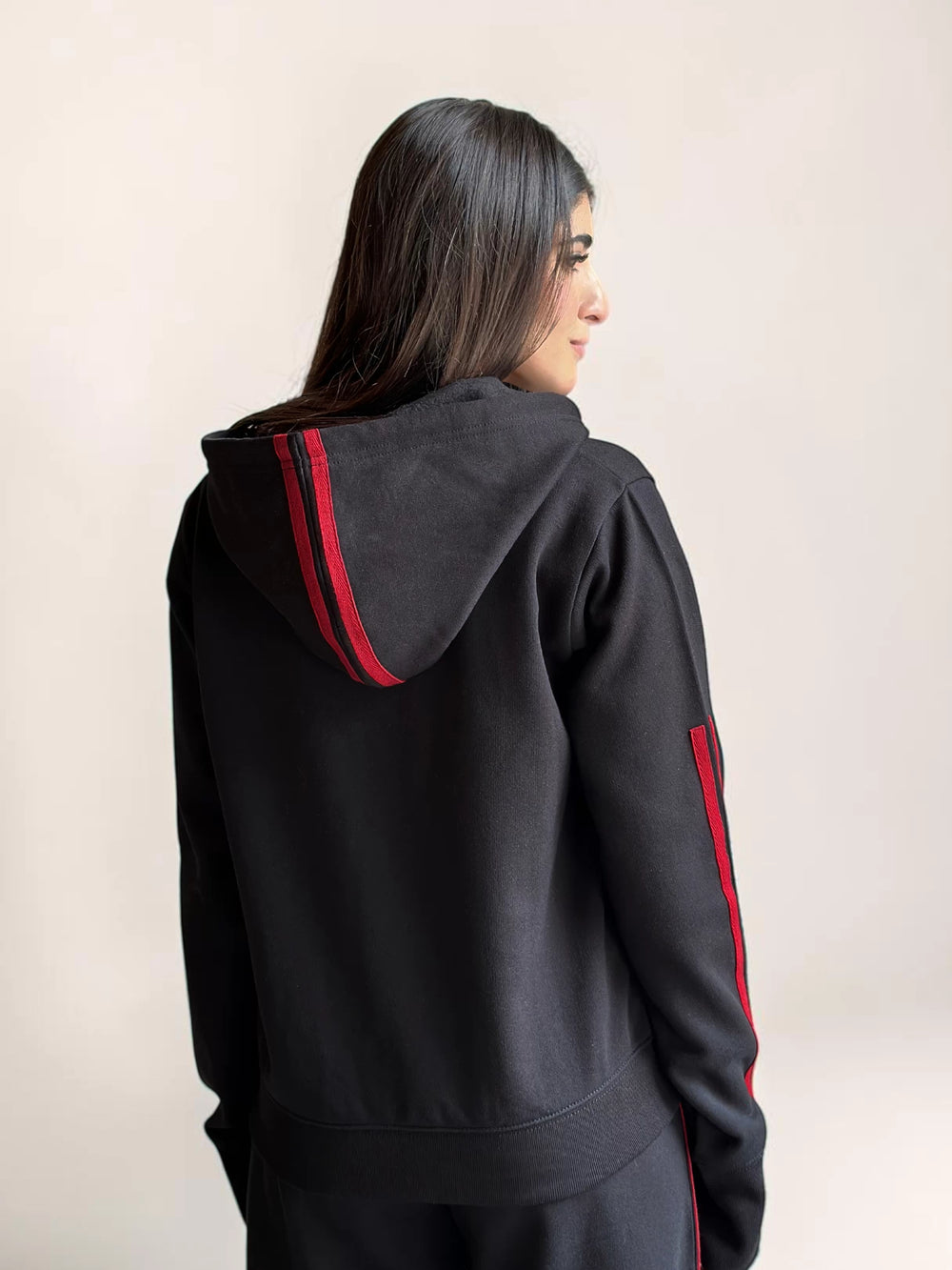 Rear view of Coastline’s black hoodie, showing the red trim around the hood and the relaxed fit across the back.