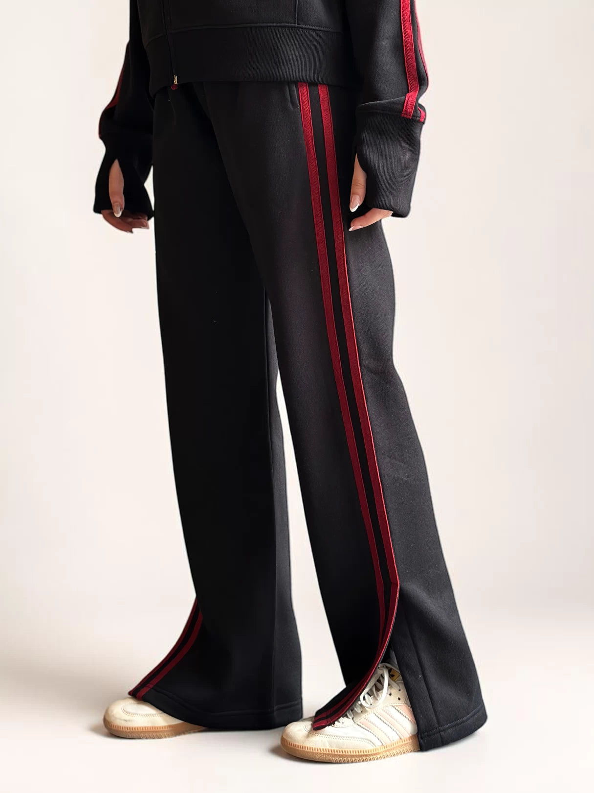 Side detail of Coastline’s black wide-leg trousers, showing the red stripes running down the outer leg and the full-length hem above cream shoes.