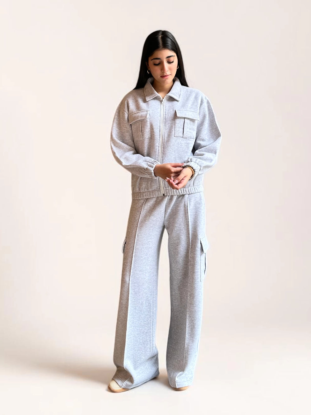 Model wearing Coastline’s heather gray fleece matching set with her hands near the waistband, showing the jacket’s gathered hem and wide-leg trouser fit.