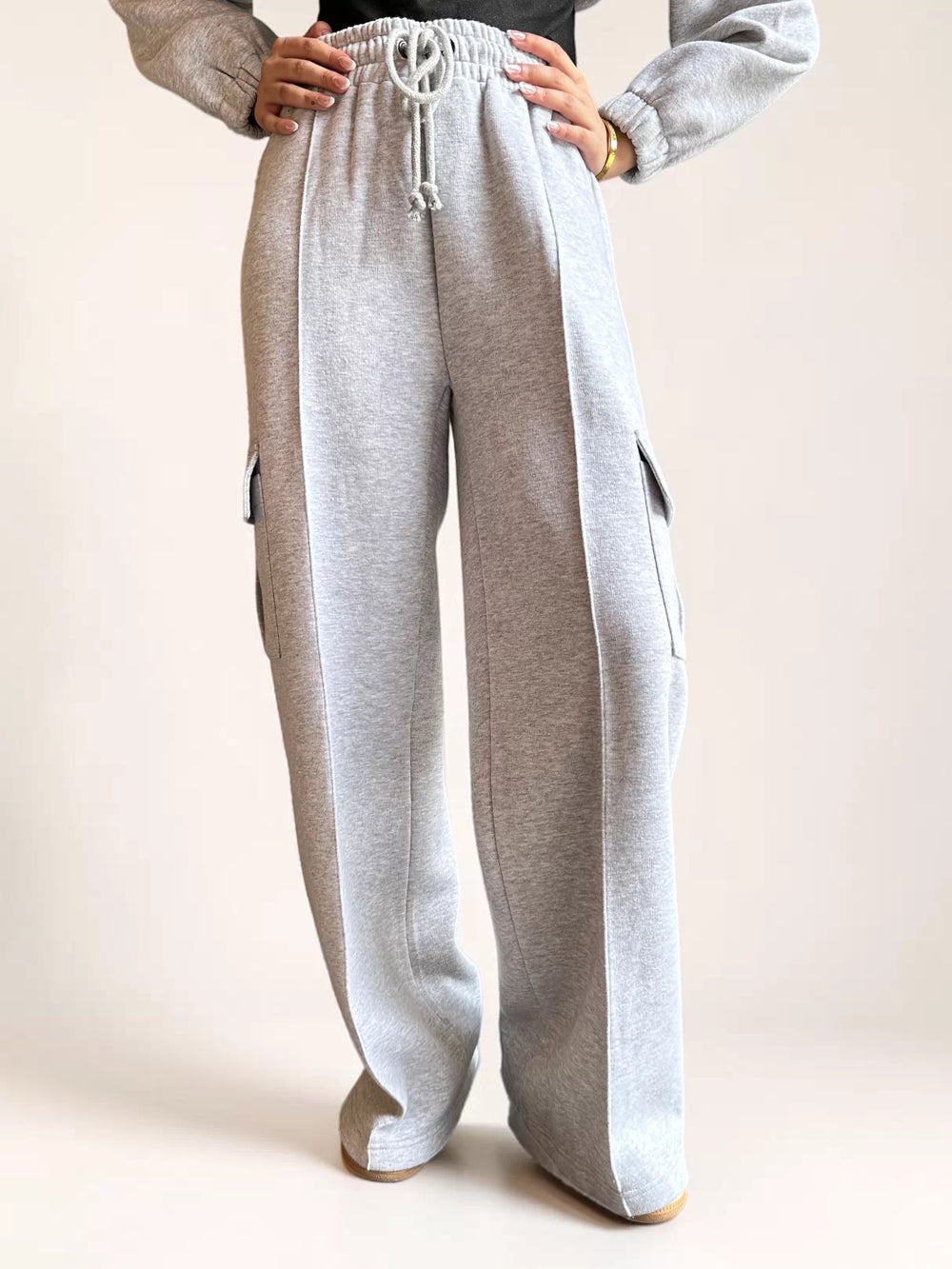Model wearing Coastline’s heather gray fleece cargo sweatpants with one hand on her hip, showing the gathered waistband and loose wide-leg silhouette.