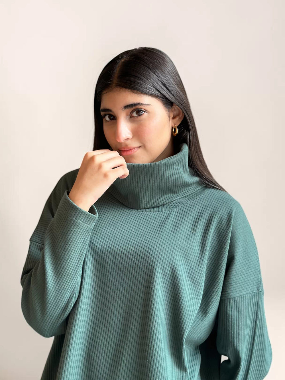 Model wearing Coastline’s Yula evergreen co-ord top with a hand near the collar, showing the high neckline and double-knit texture.