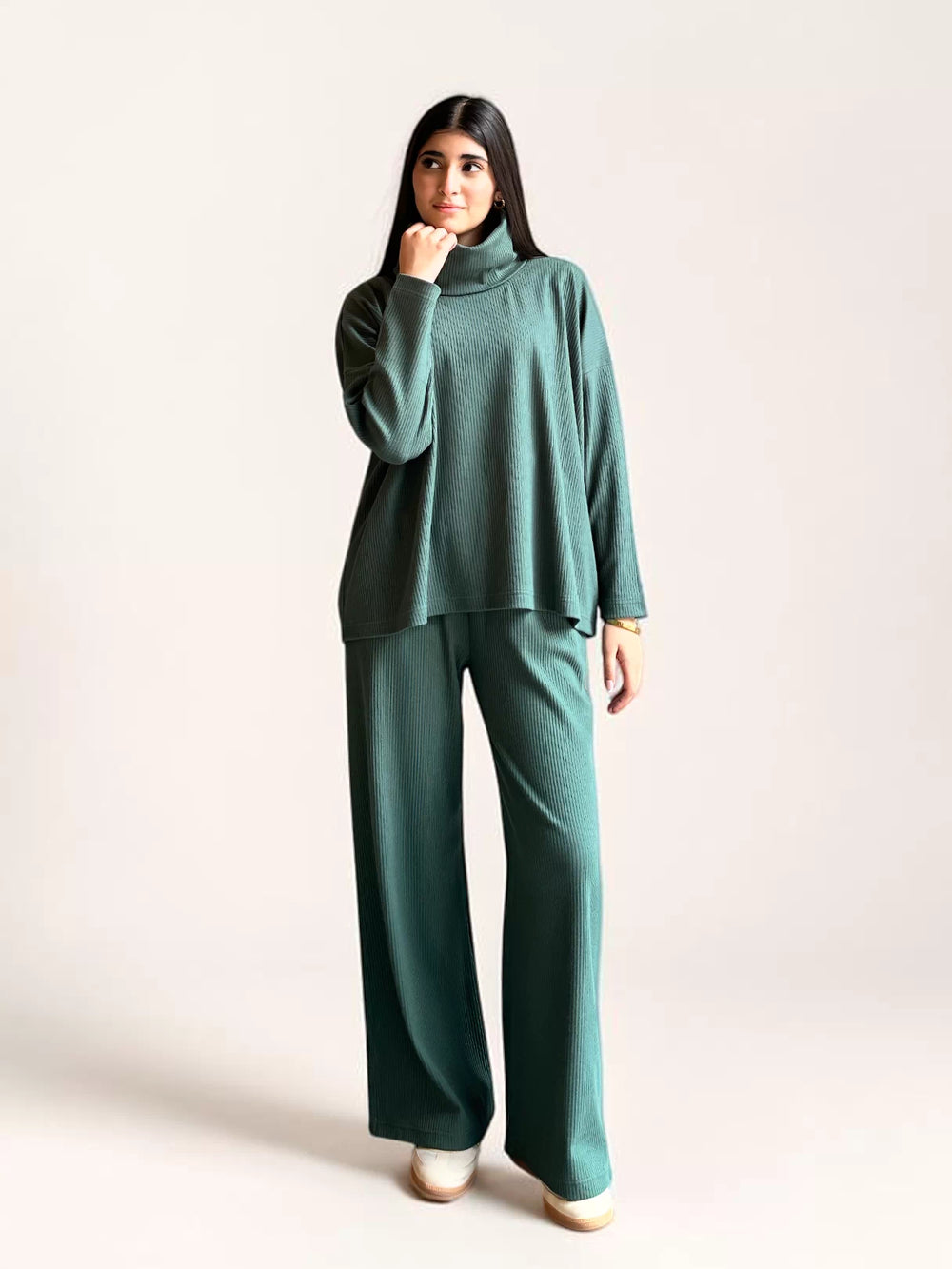 Full-length view of a model wearing Coastline’s Yula evergreen co-ord set, with one hand raised near the high neckline.