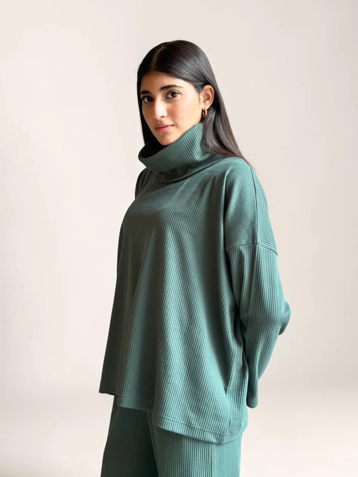 Side view of a model wearing Coastline’s Yula evergreen double-knit co-ord top, showing its high neckline, loose sleeves and relaxed drape.