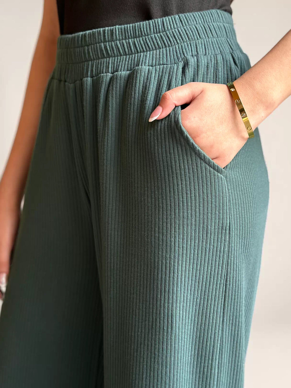 Close-up of Coastline’s Yula evergreen double-knit trousers, showing the gathered waistband and a hand in the side pocket.