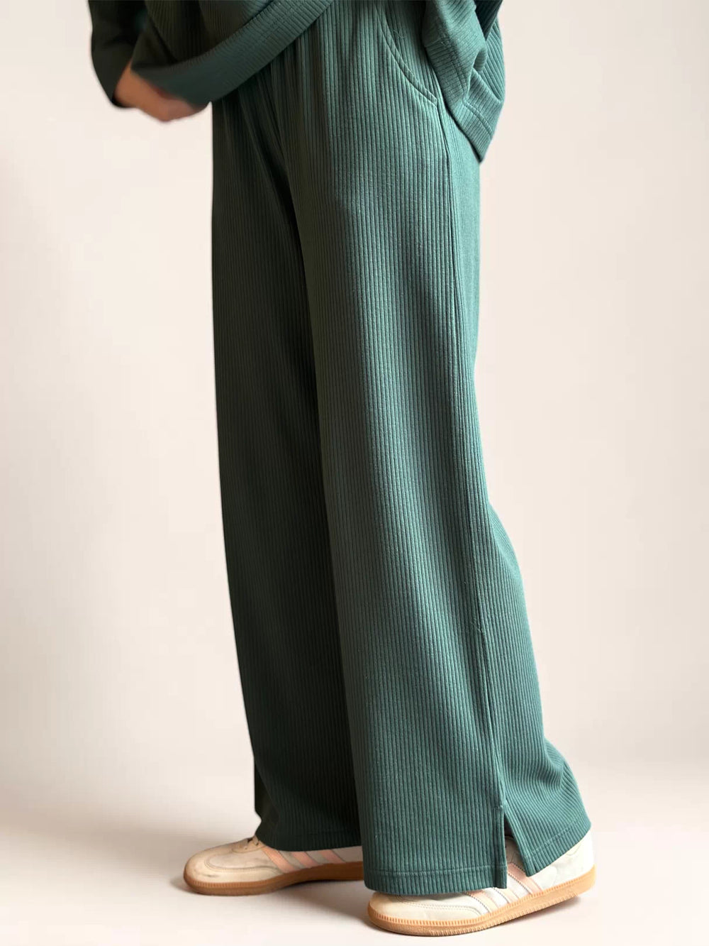 Side detail of Coastline’s Yula evergreen double-knit trousers, showing the wide-leg silhouette and full-length hem above cream shoes.