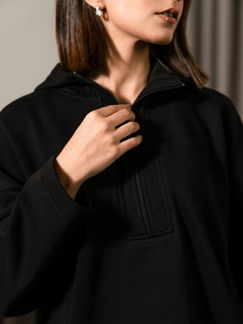 Closer view of the Darya black hoodie with the model holding the neckline beside the front zipper.