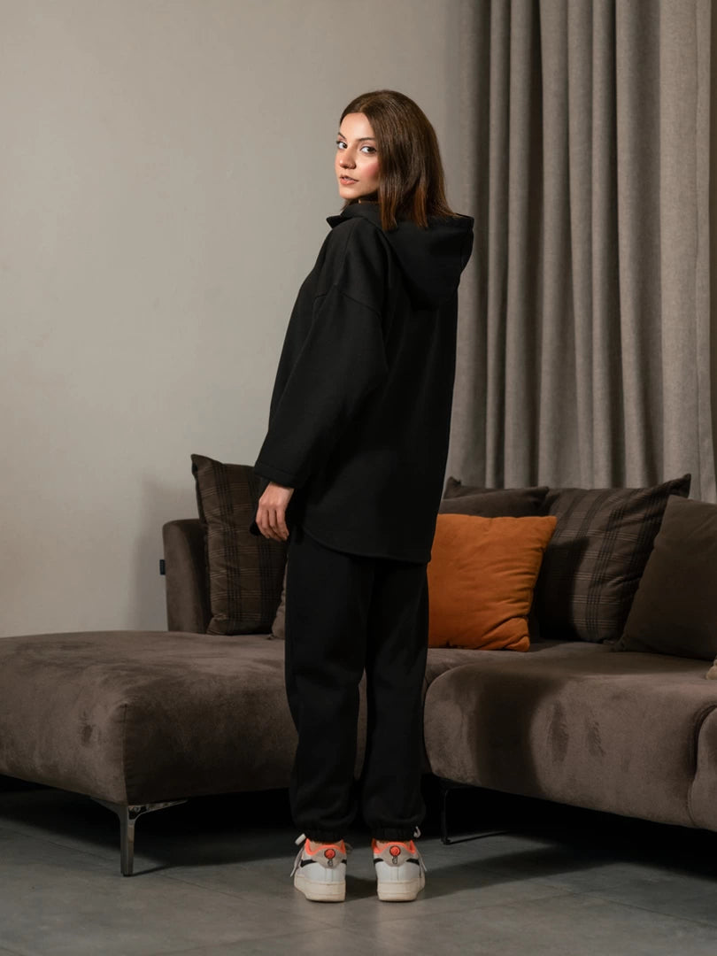 Angled side view of the Darya black winter co-ord set showing the loose hoodie silhouette and long hem over the trousers.
