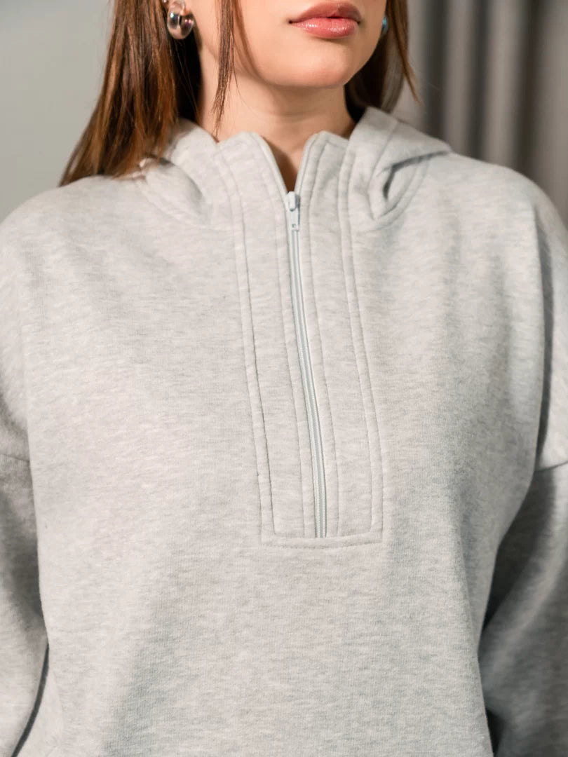 Closer view of the Darya Heather Grey oversized hoodie showing the extended zipper and front pockets, with both hands in the pockets.